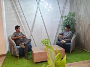 Two professionals in casual conversation in a stylish, plant-filled office space.