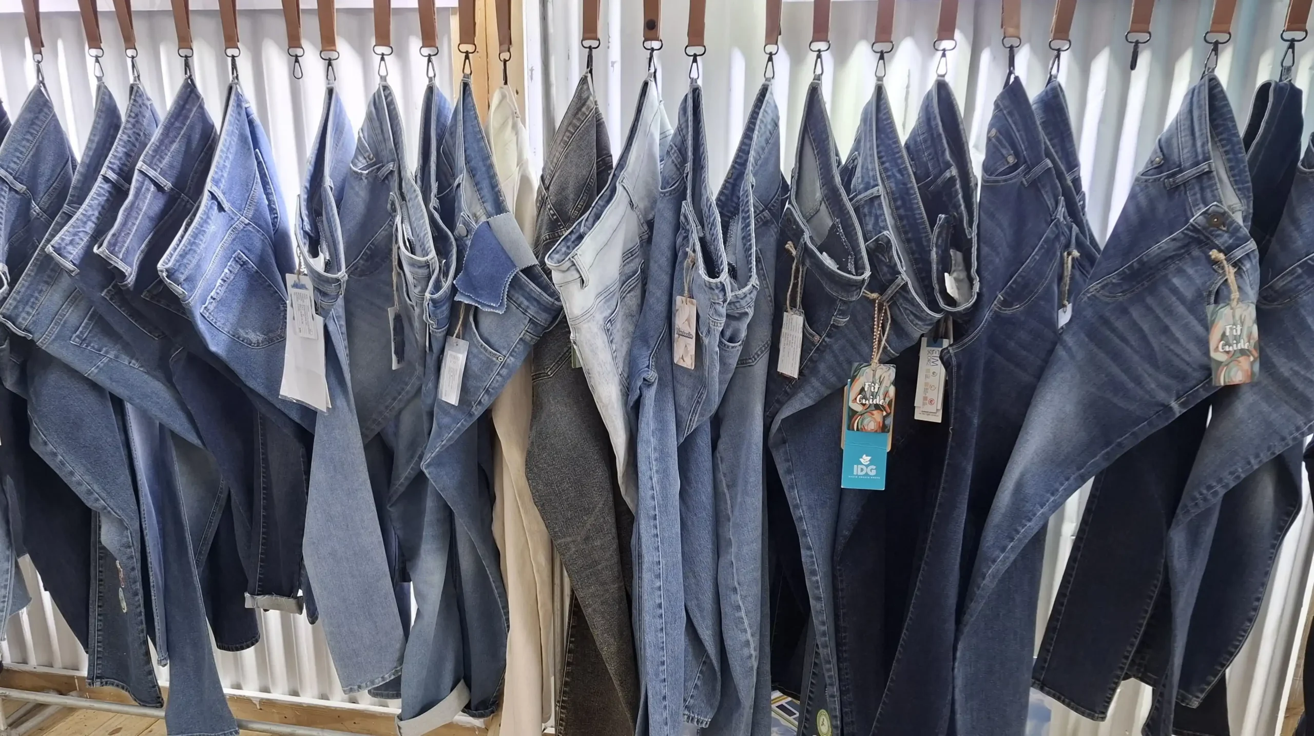 Various denim jeans in different washes and styles hanging on a rack at a fashion sourcing exhibition