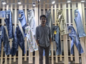 Antor Hossain standing confidently amidst a display of diverse denim jeans and casual pants at a fashion expo in Dhaka.