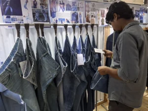 Antor Hossain standing among mannequins displaying various denim and casual apparel at a fashion exhibition or showroom.