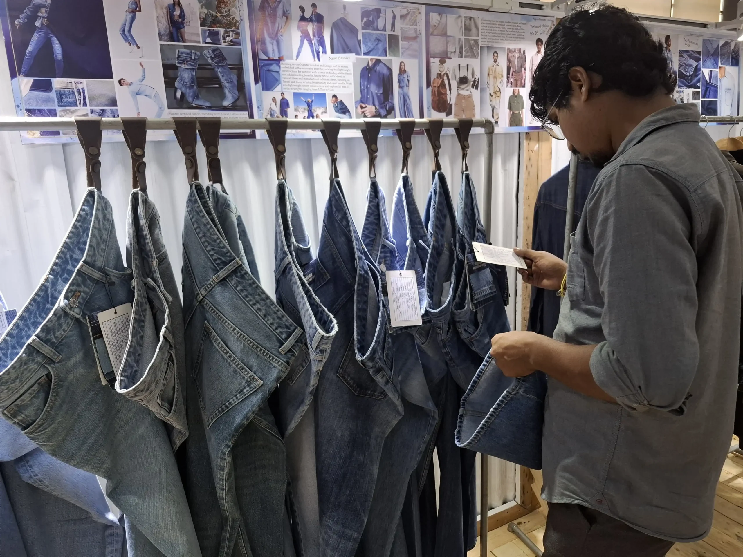 Antor Hossain standing among mannequins displaying various denim and casual apparel at a fashion exhibition or showroom.