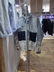 Light blue denim-style shirt with dark patterned patch pockets on a clothing rack.