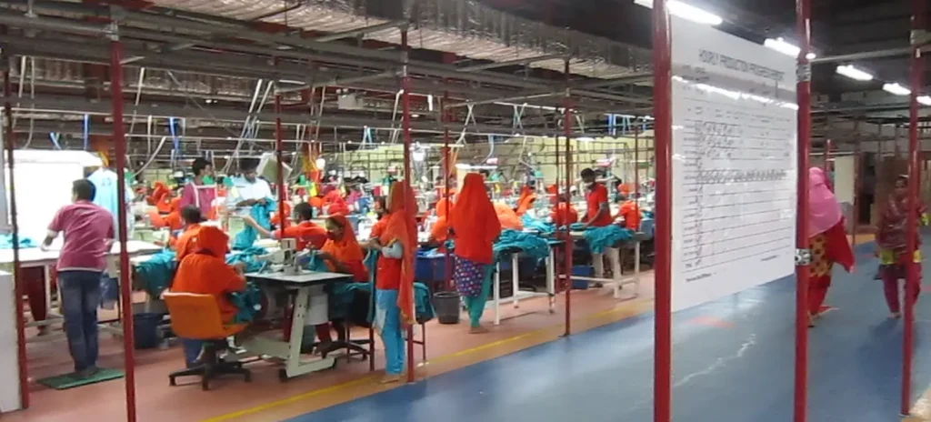 Bangladesh garment factory sewing line with workers in orange uniforms on the production floor